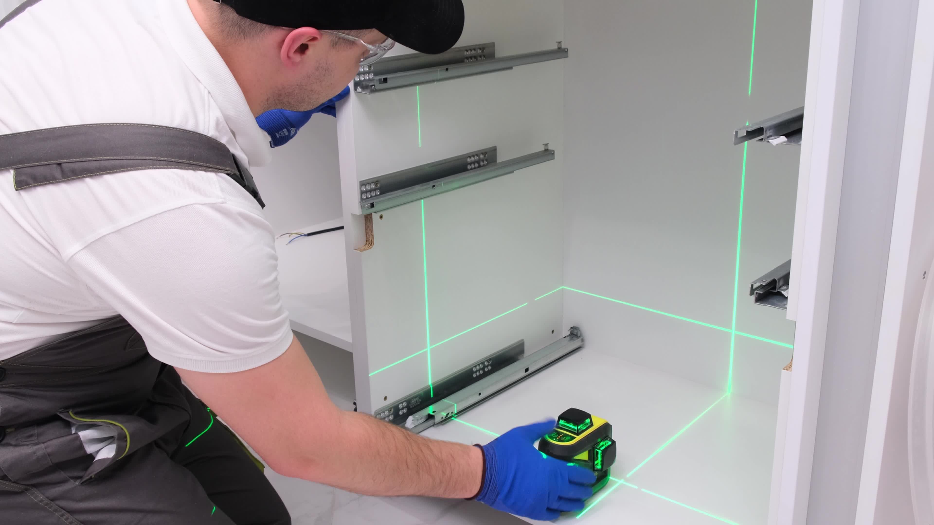 man uses a laser level to install cabinetry