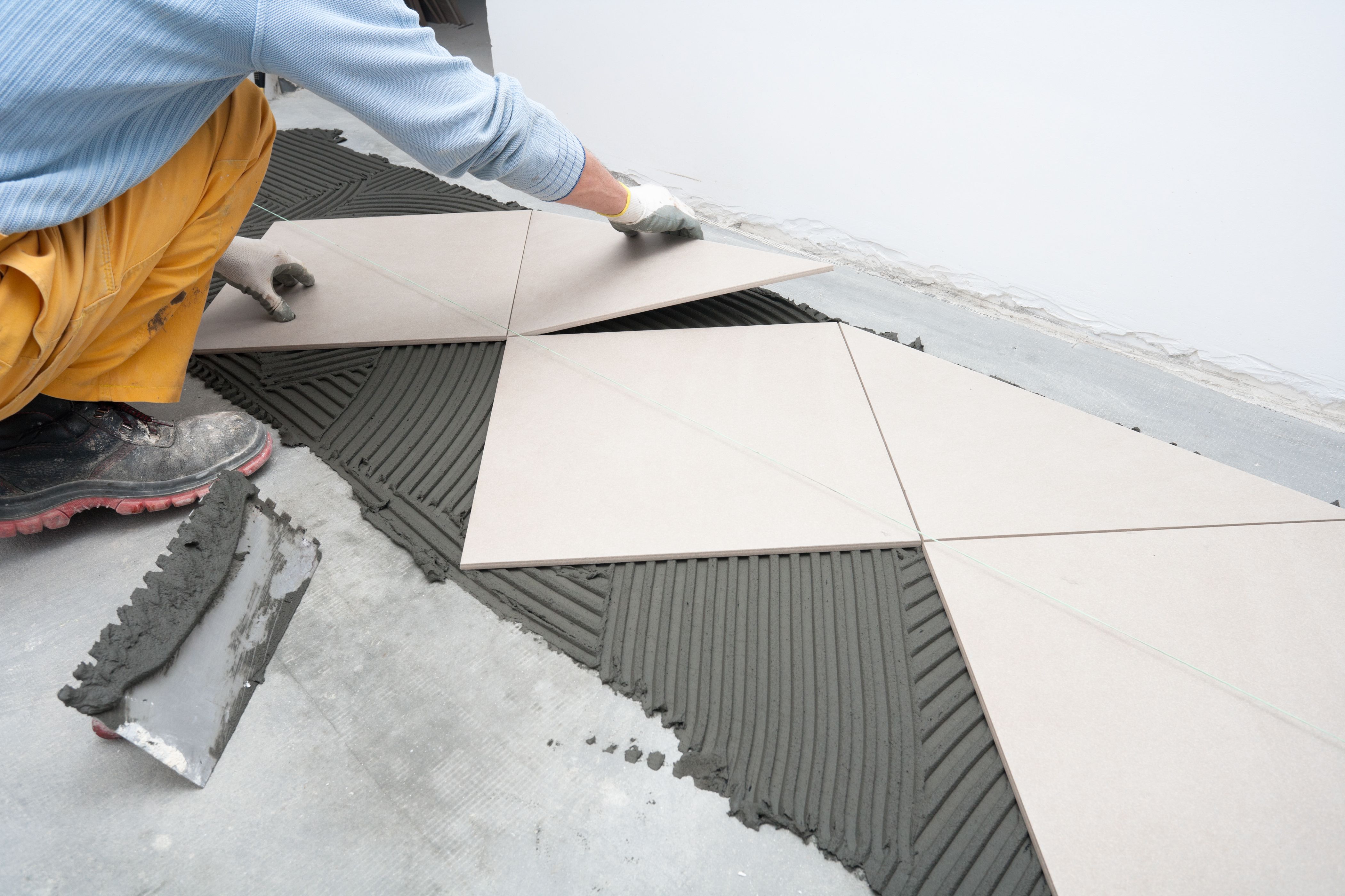 person laying white tiles into the flooring compound